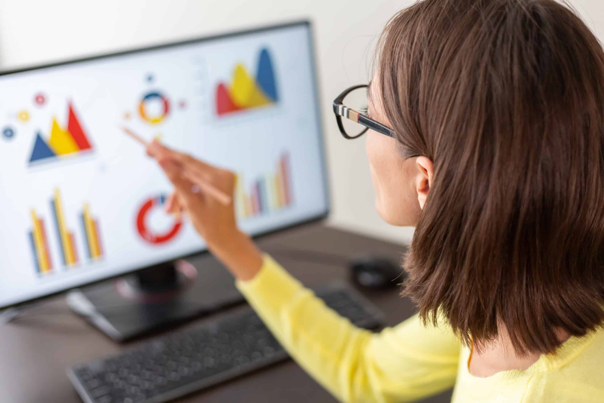 Mulher analisando gráficos em tela de computador durante uma auditoria de marketing digital, avaliando desempenho e métricas de canais digitais.
