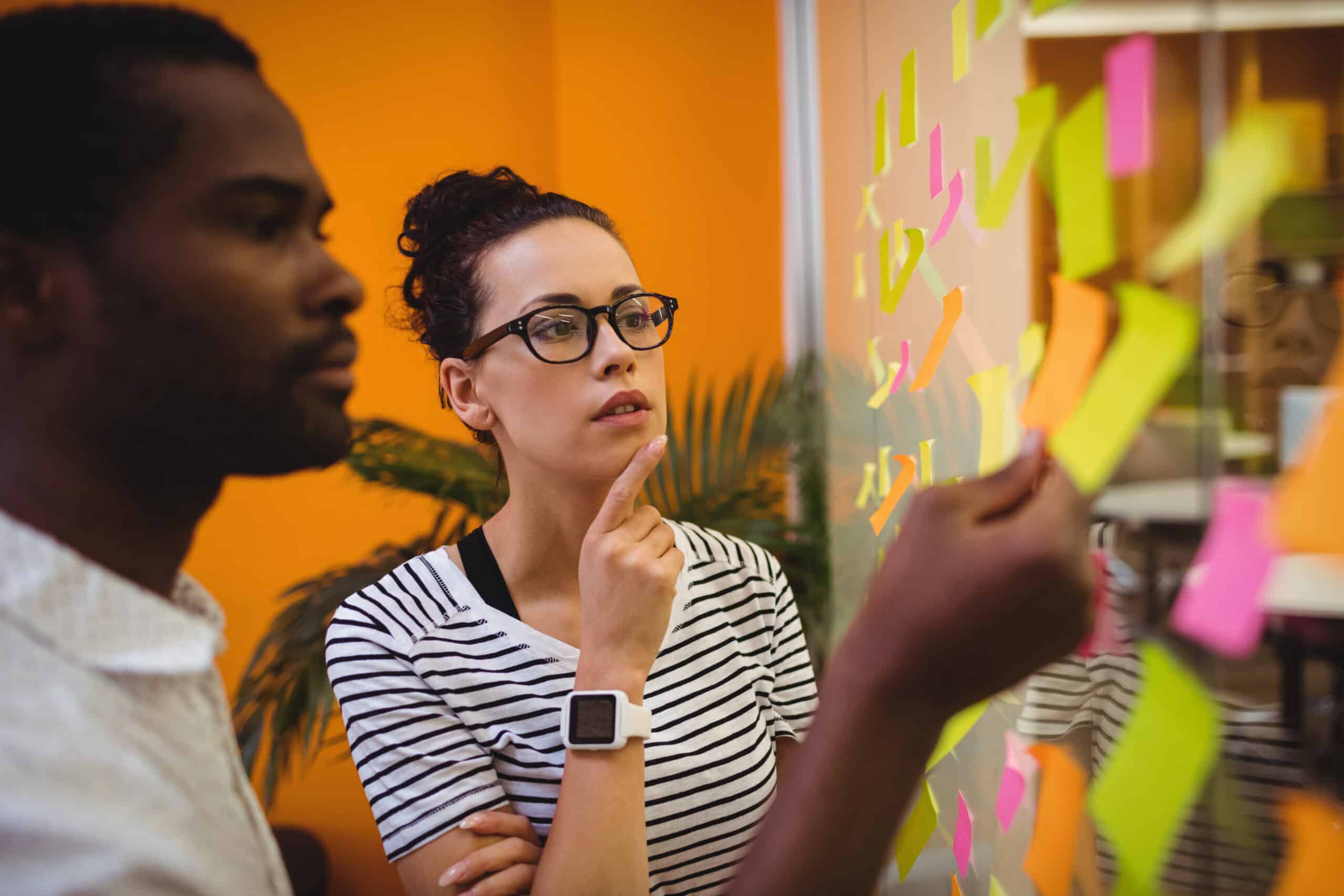 Dois profissionais analisando post-its coloridos em um quadro de planejamento, representando o desenvolvimento de habilidades de marketing digital