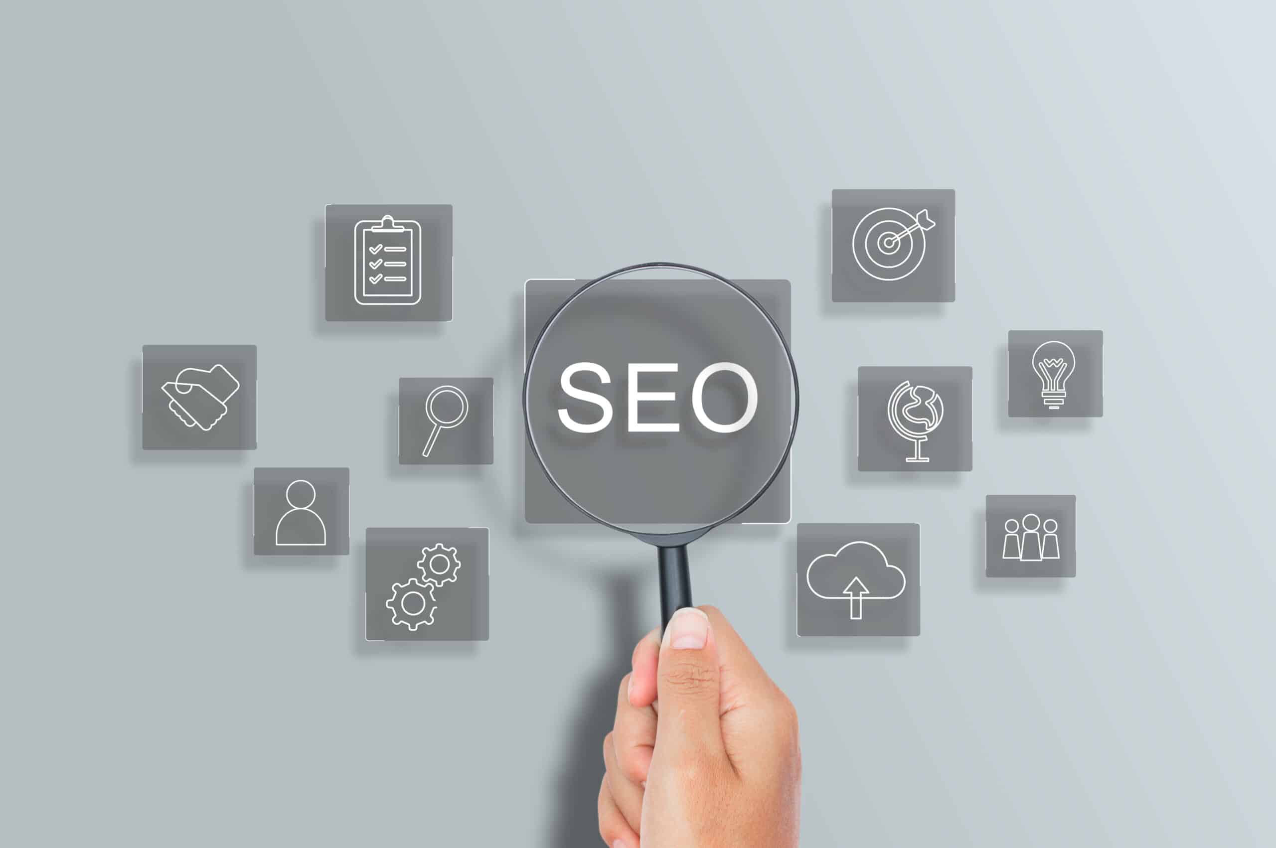 Mão segurando lupa destacando a palavra SEO entre ícones digitais, representando otimização de sites e estratégias de marketing digital.