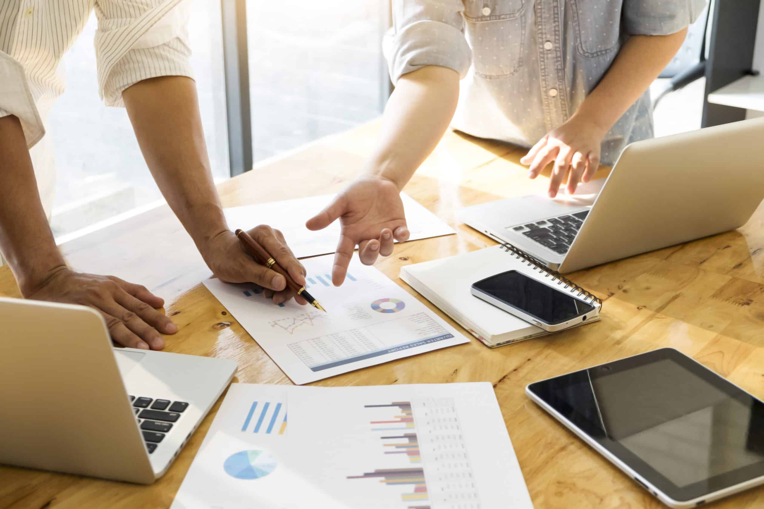 Duas pessoas analisando gráficos e relatórios de desempenho em laptops durante uma reunião de planejamento de marketing para a Black Friday.